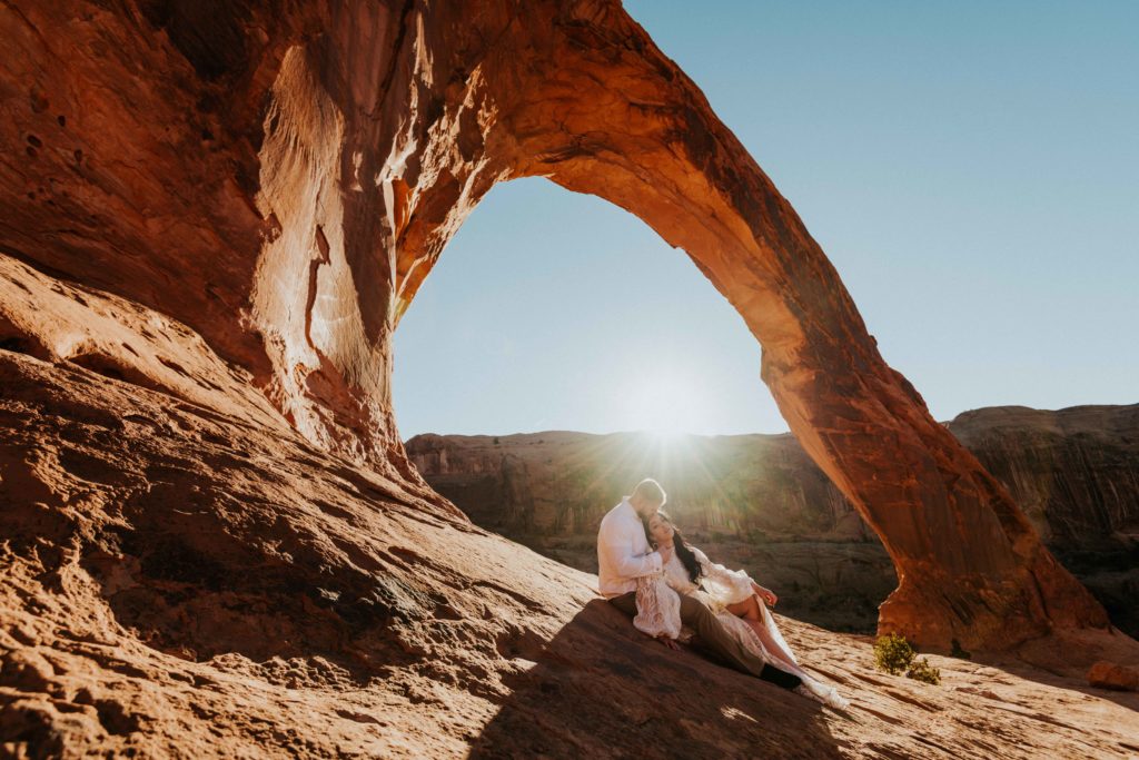 Couple sitting under an arch in Moab Utah.
